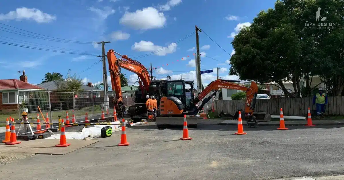 Construction site with diggers, cones, and workers in residential area.